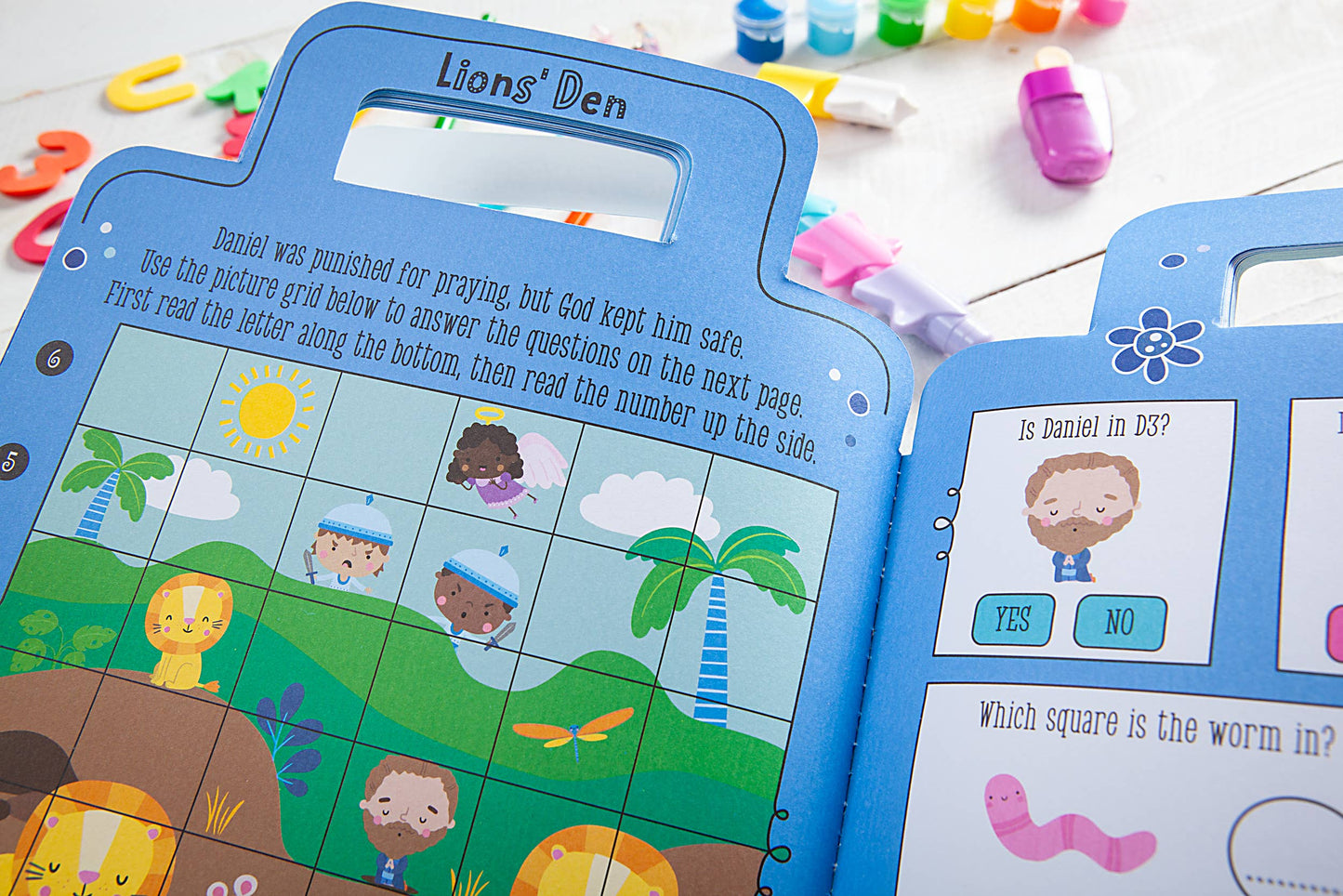 Children's blue activity books on a wooden surface with paint and toys.