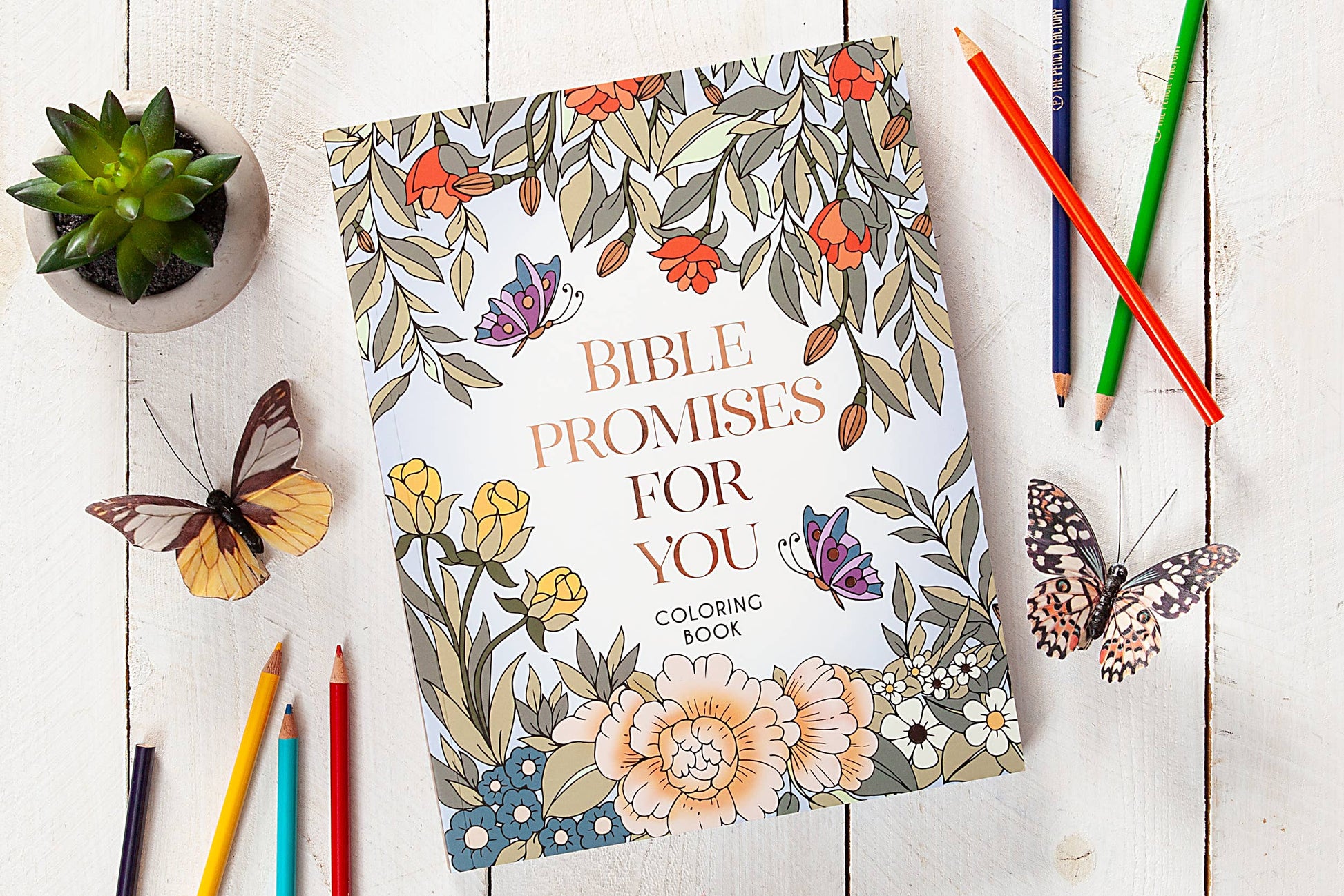 Bible Promises Coloring book with a floral design and text, surrounded by colored pencils on a wooden surface.