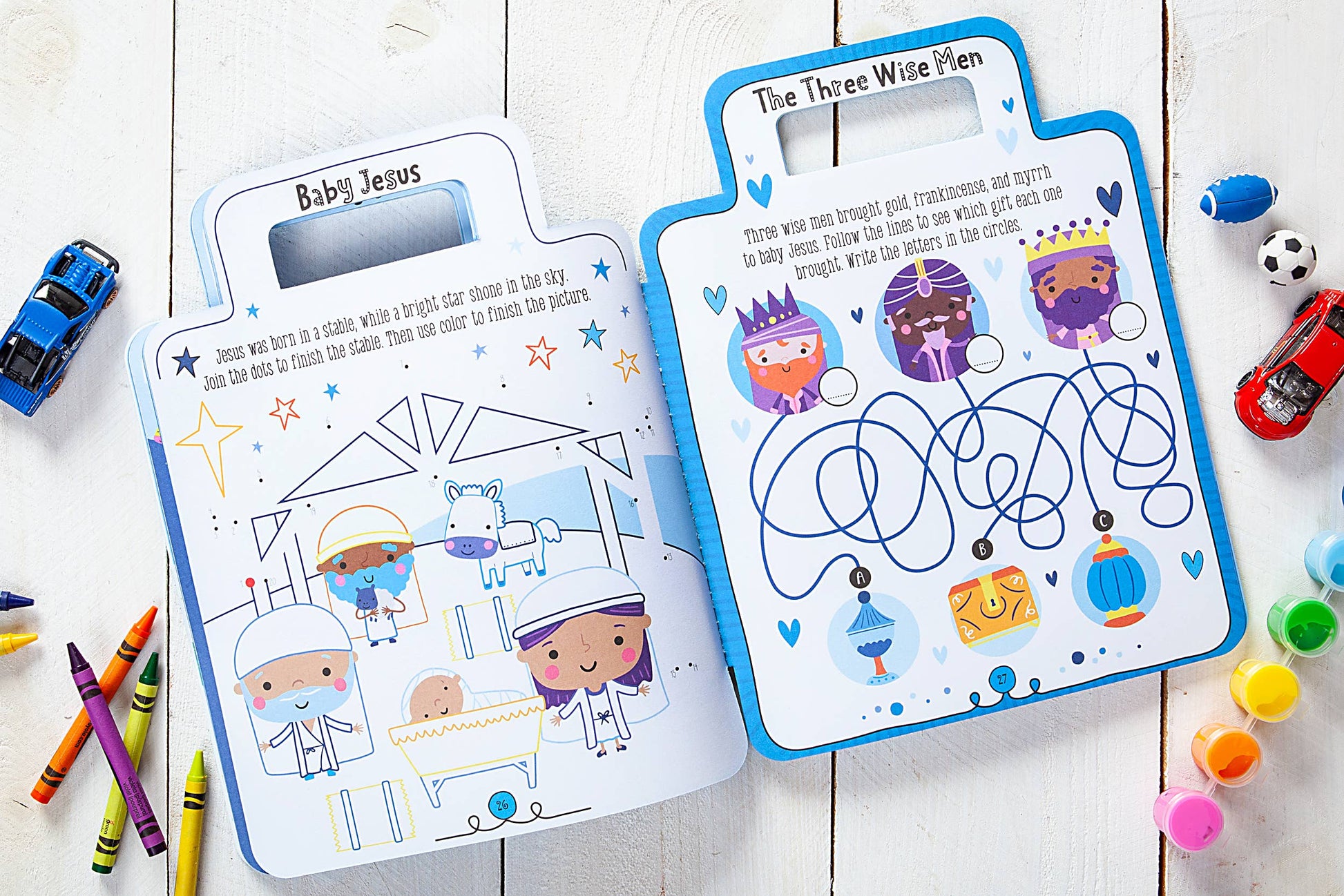 Blue children's activity book on a wooden surface with crayons and toys.