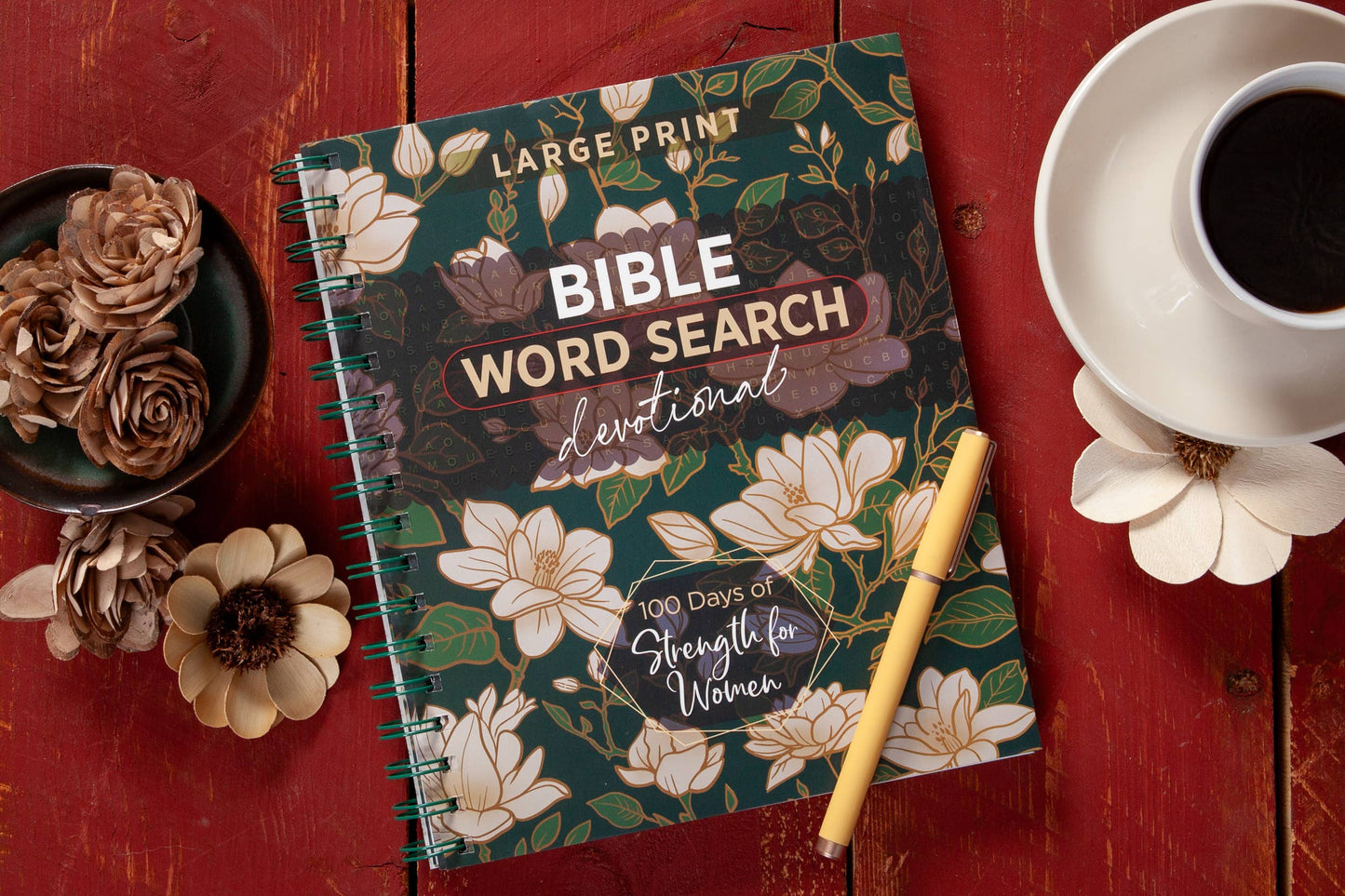 Large print floral devotional word search book on a table with  various objects surrounding the book.