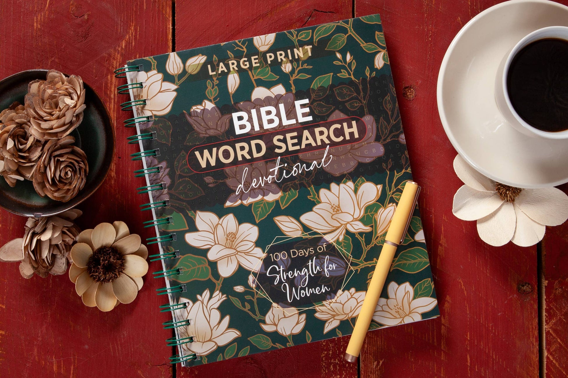 Large print floral devotional word search book on a table with  various objects surrounding the book.