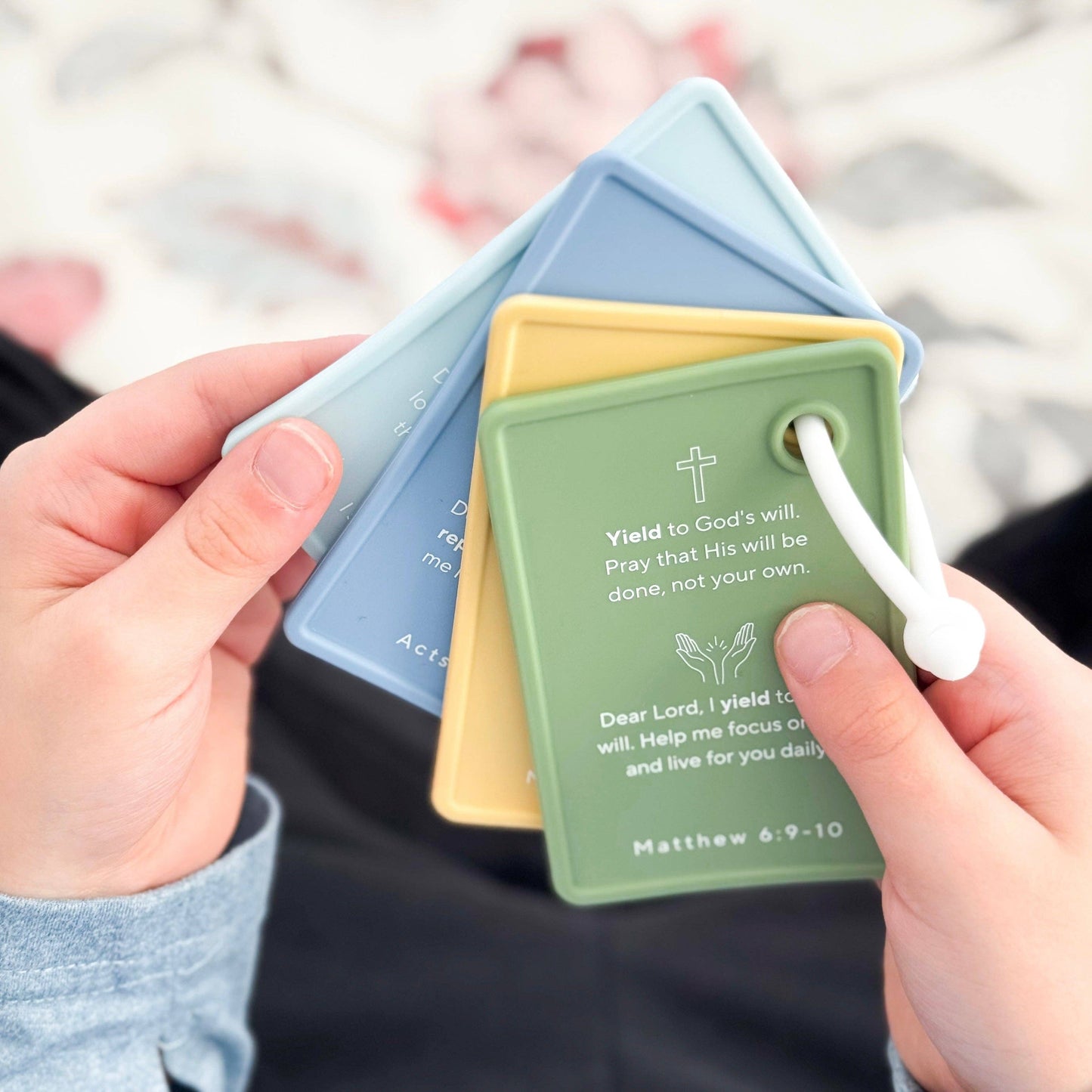 Hands holding a stack of prayer cards with a cross symbol and text.