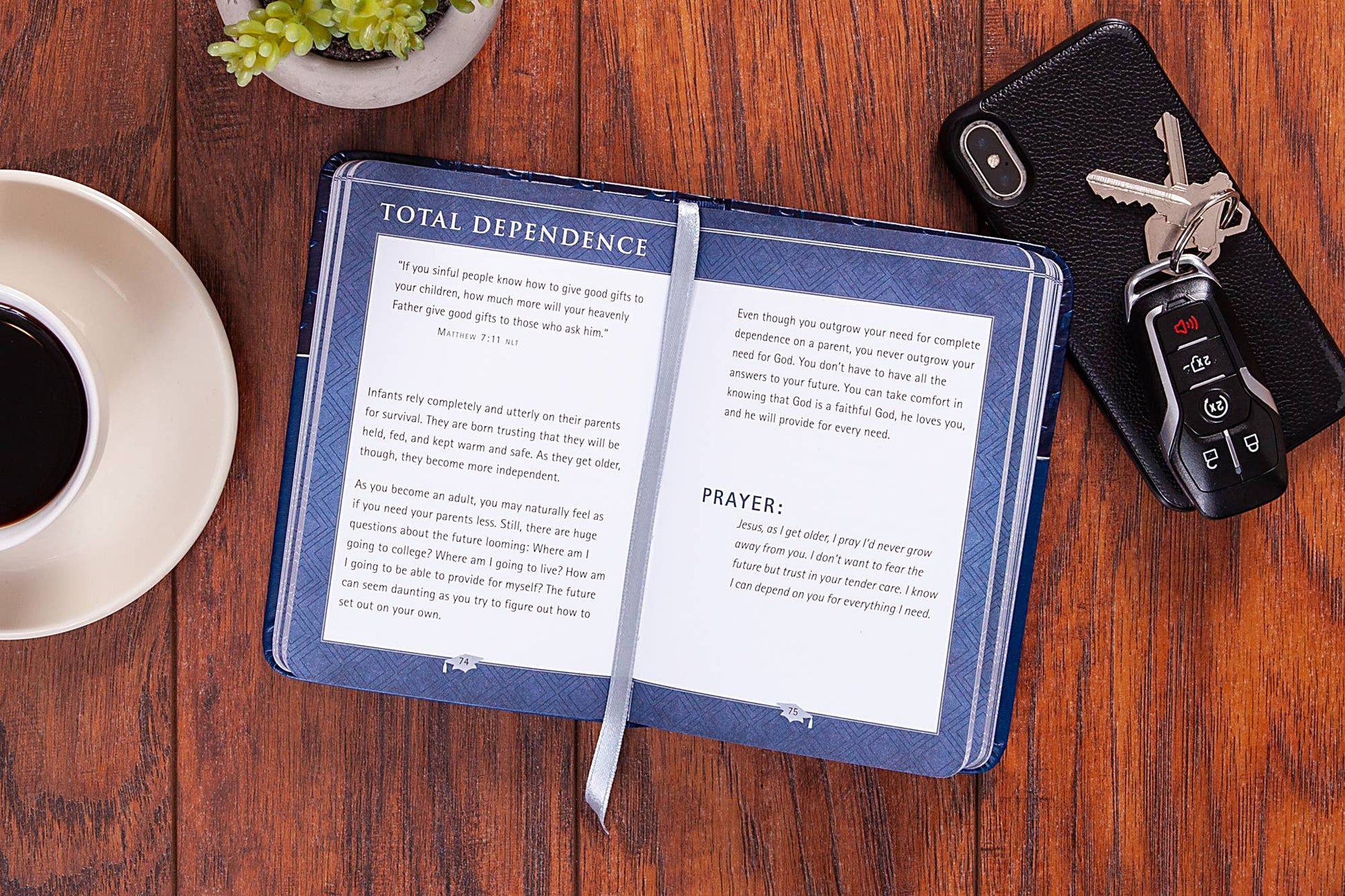 Open book  on a wooden table with a cup of coffee, keys, and a plant.