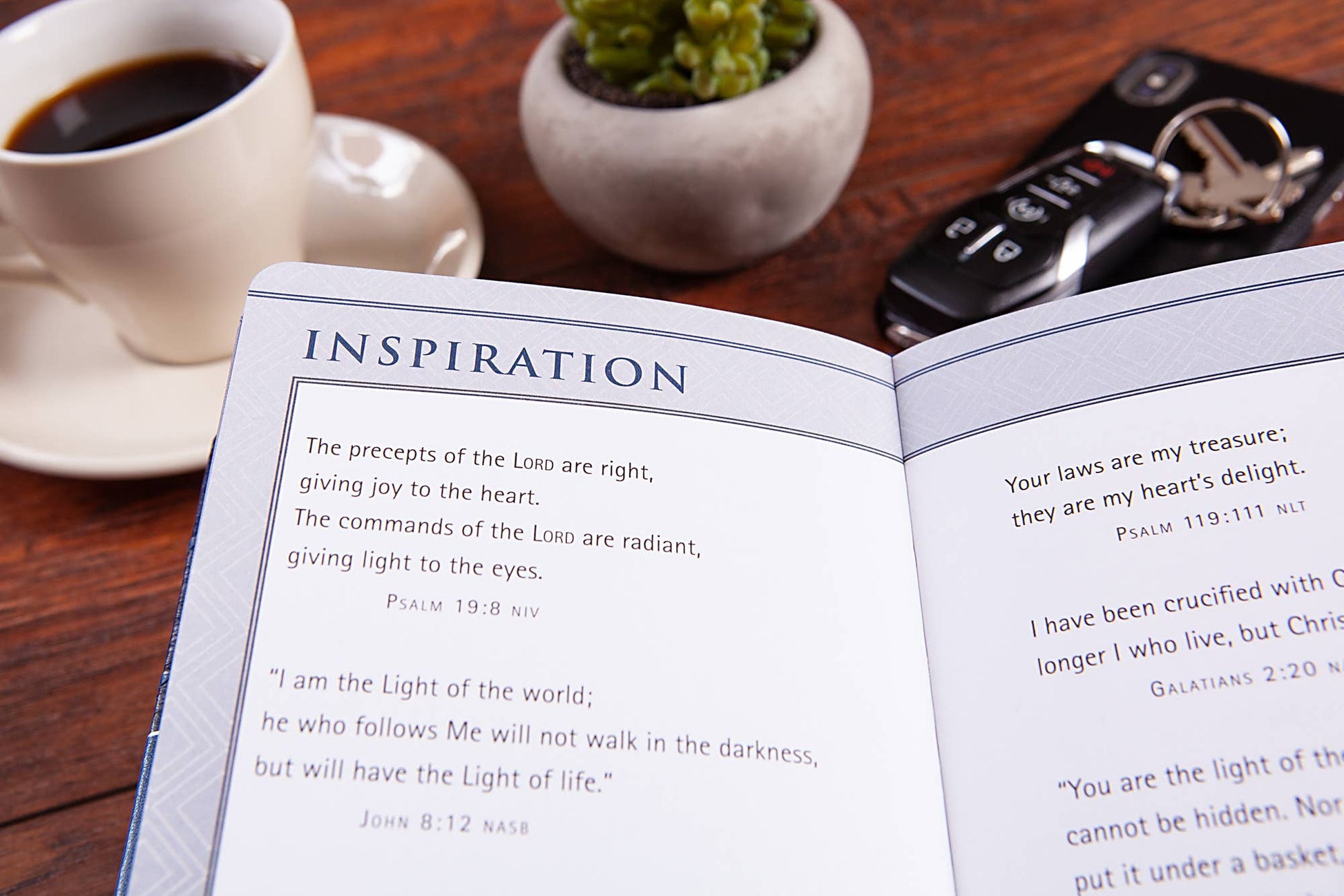 Open book  on a wooden table with a cup of coffee, keys, and a plant.