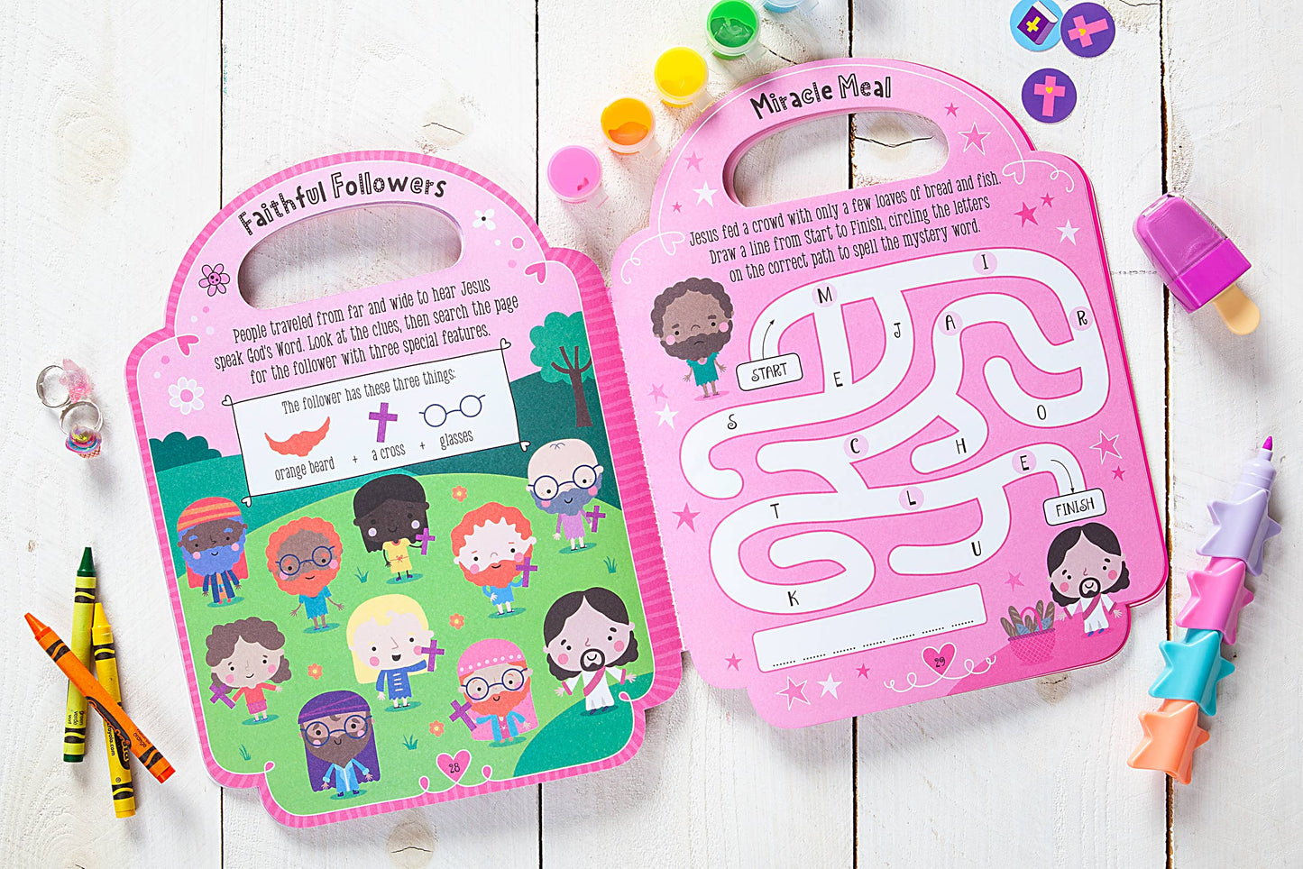 Children's pink activity books on a wooden surface with crayons and stickers.