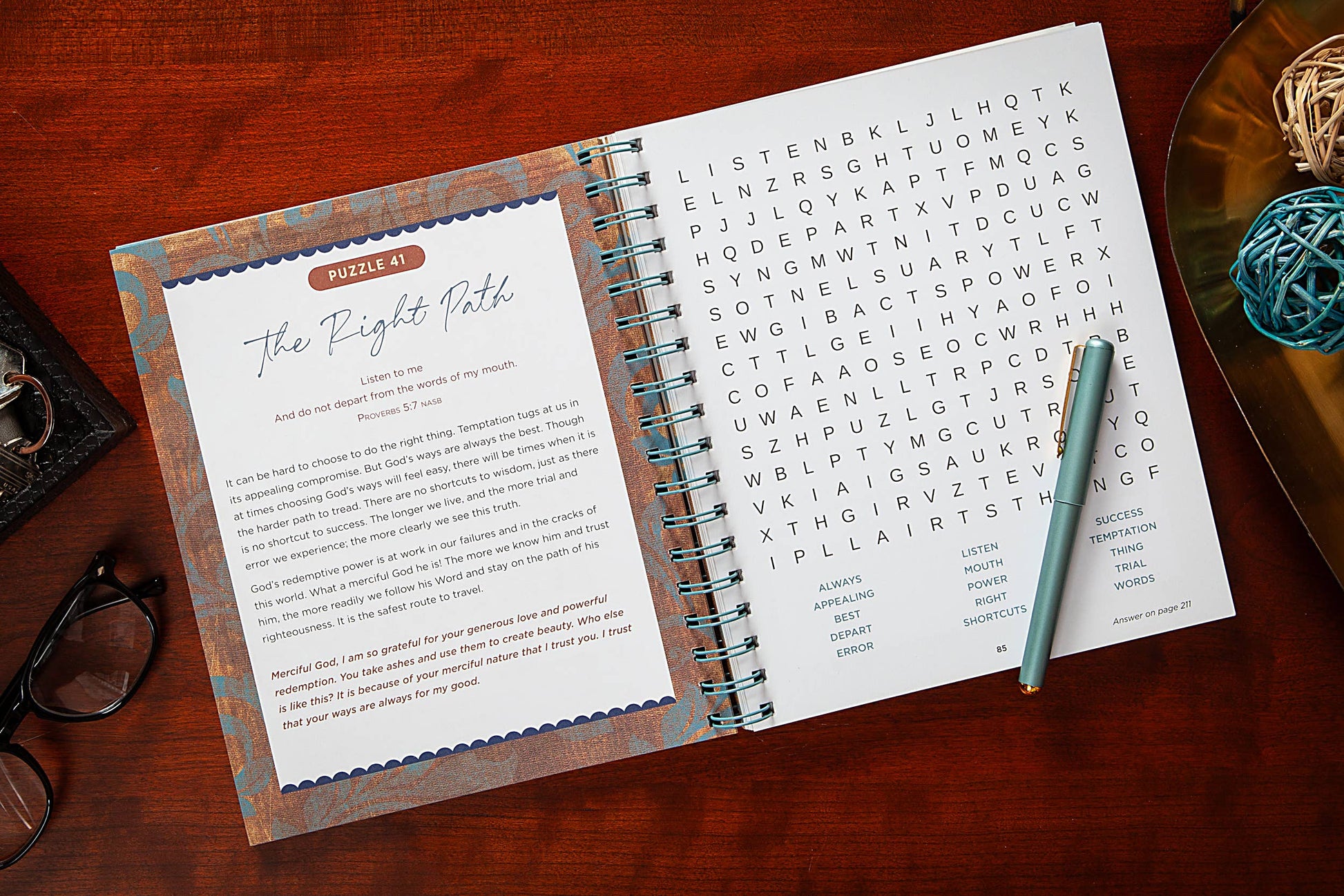 Open Bible Word Search devotional book on a wooden surface with a pen and phone.