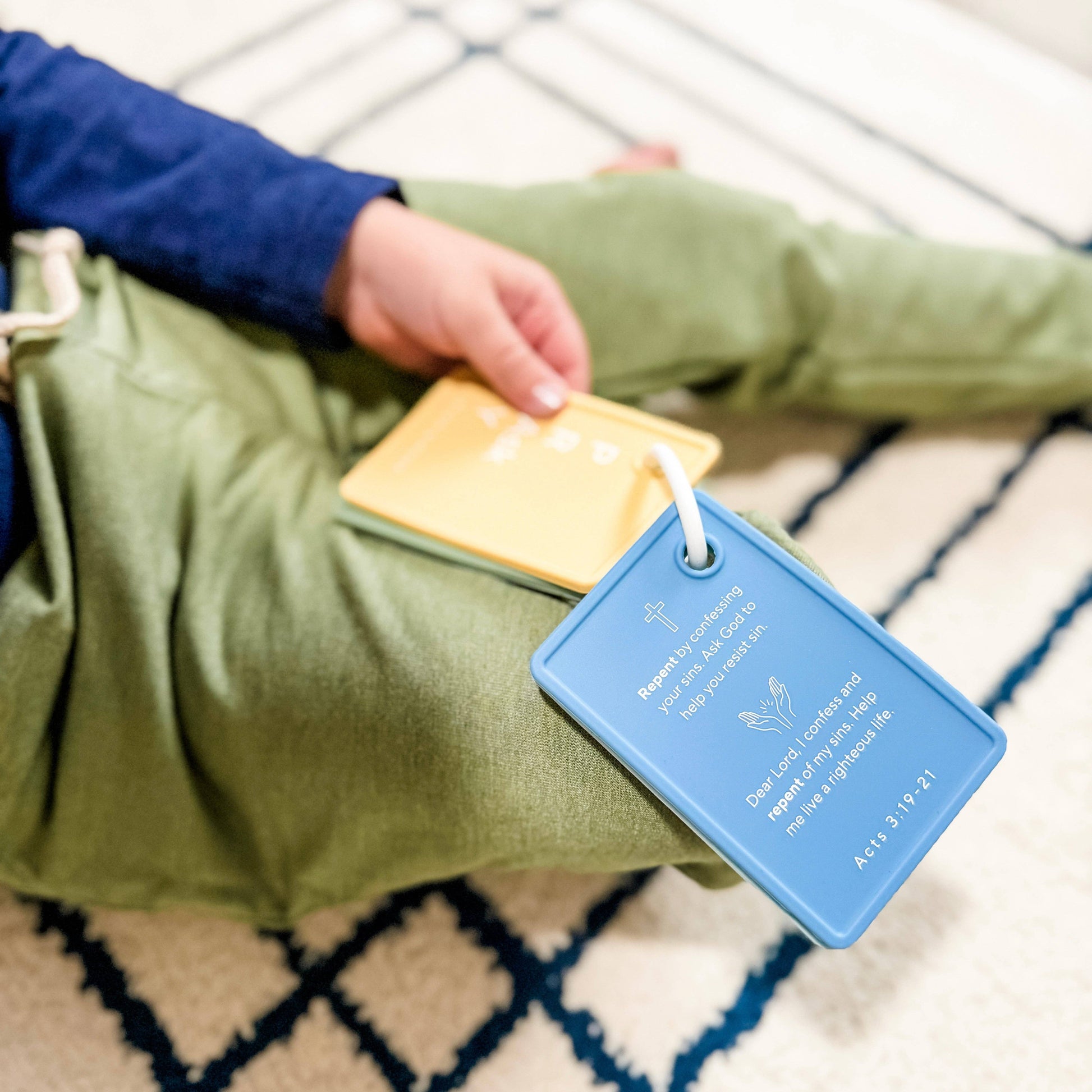 Person holding a green bag with a blue tag featuring text and a date, on a patterned rug.