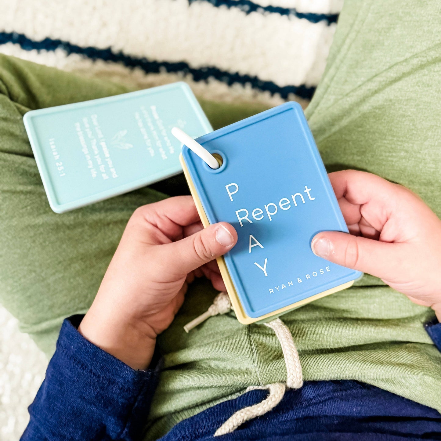 Person holding a blue card with 'P Repent' text, sitting on a striped surface.