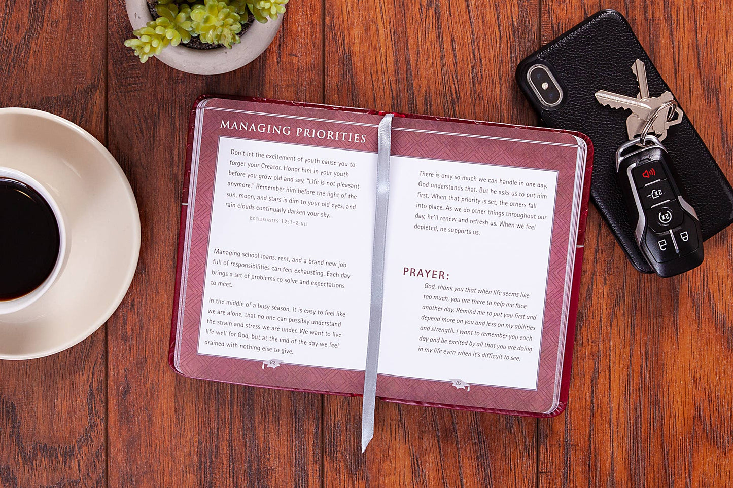 Open notebook on a wooden table with a cup of coffee, keys, and a plant.