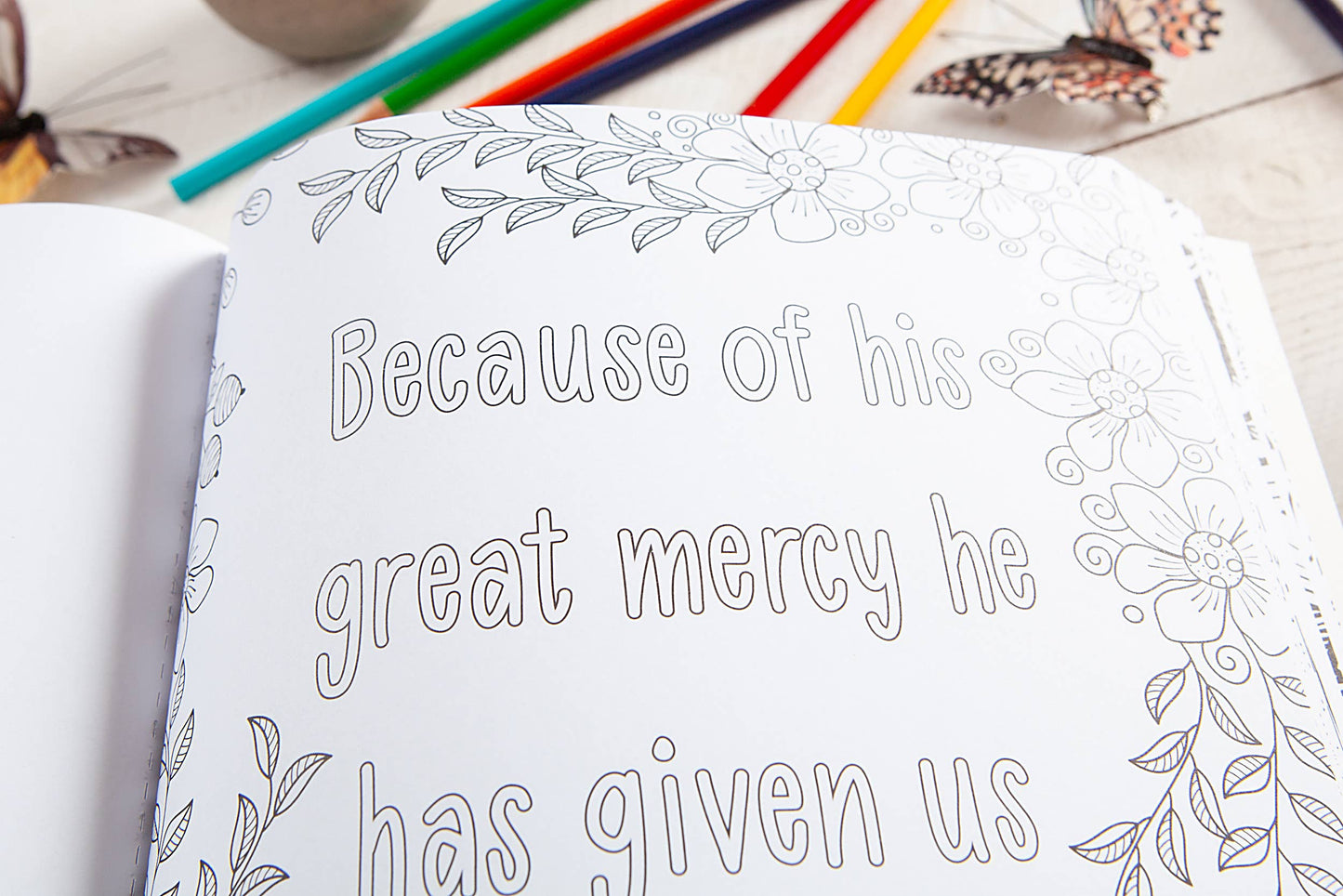 Coloring book with a floral design and text, surrounded by colored pencils on a wooden surface.