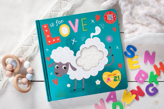 Children's book titled 'L is for Love' with a sheep illustration, surrounded by colorful letters and a wooden toy on a white surface.