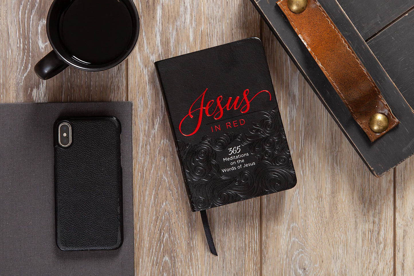 Black book with 'Jesus in Red' on a wooden surface with a phone and mug.