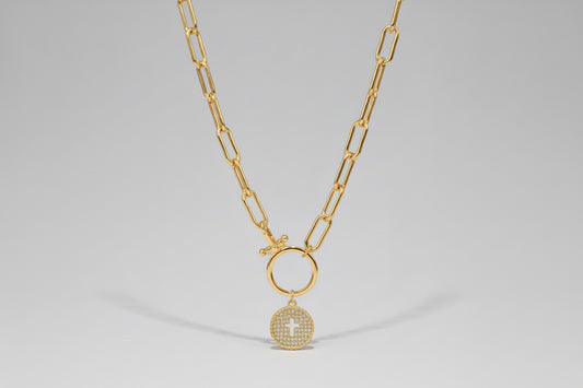 Silver necklace with a circular pendant featuring a cross on a wooden surface