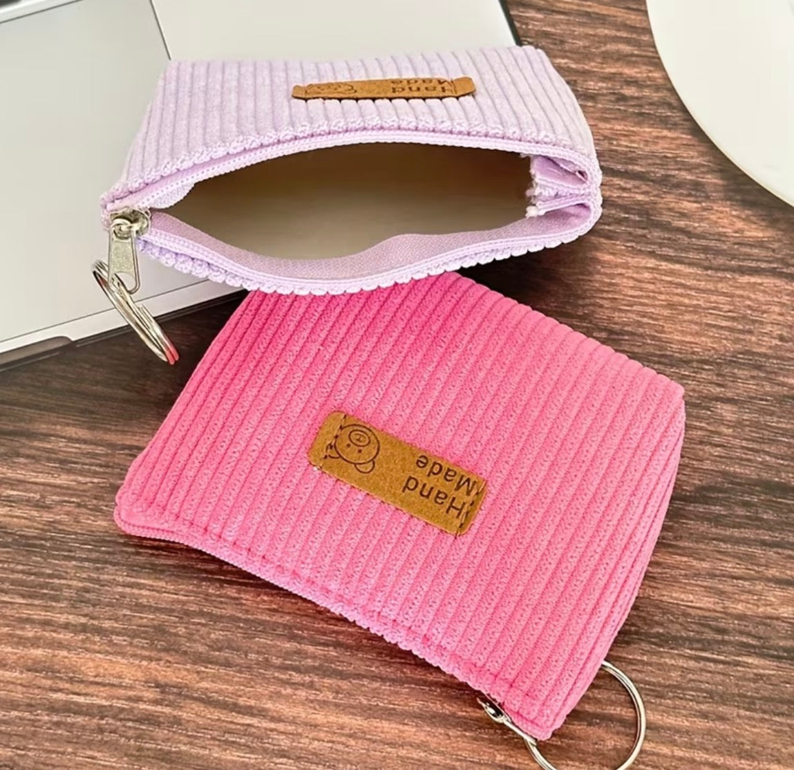 Two corduroy coin purses with attached keyring and zipper closure. One is pink and one id light purple
