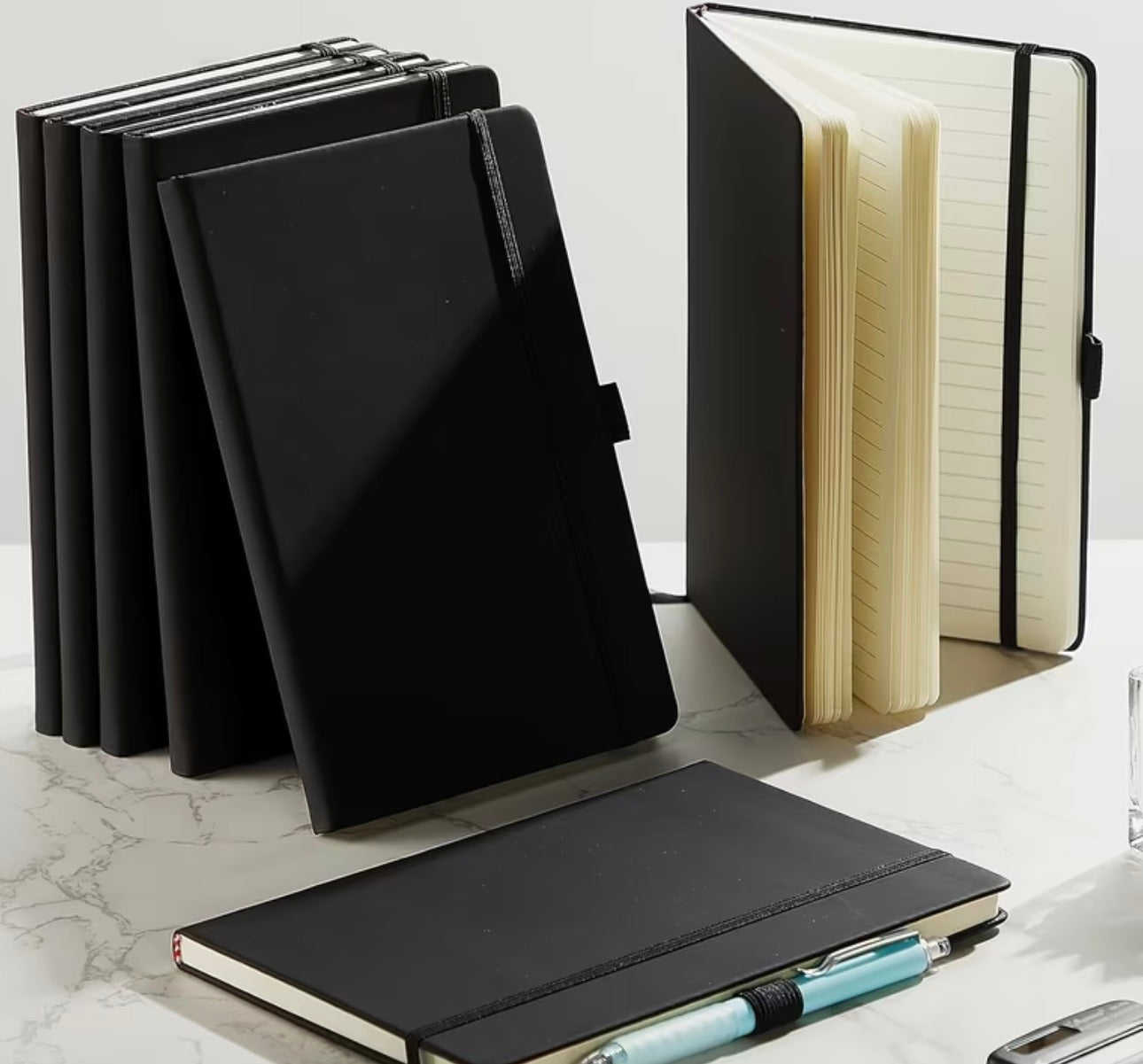 Black notebooks on a marble surface with one open to show lined pages.