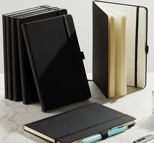 Black notebooks on a marble surface with one open to show lined pages.