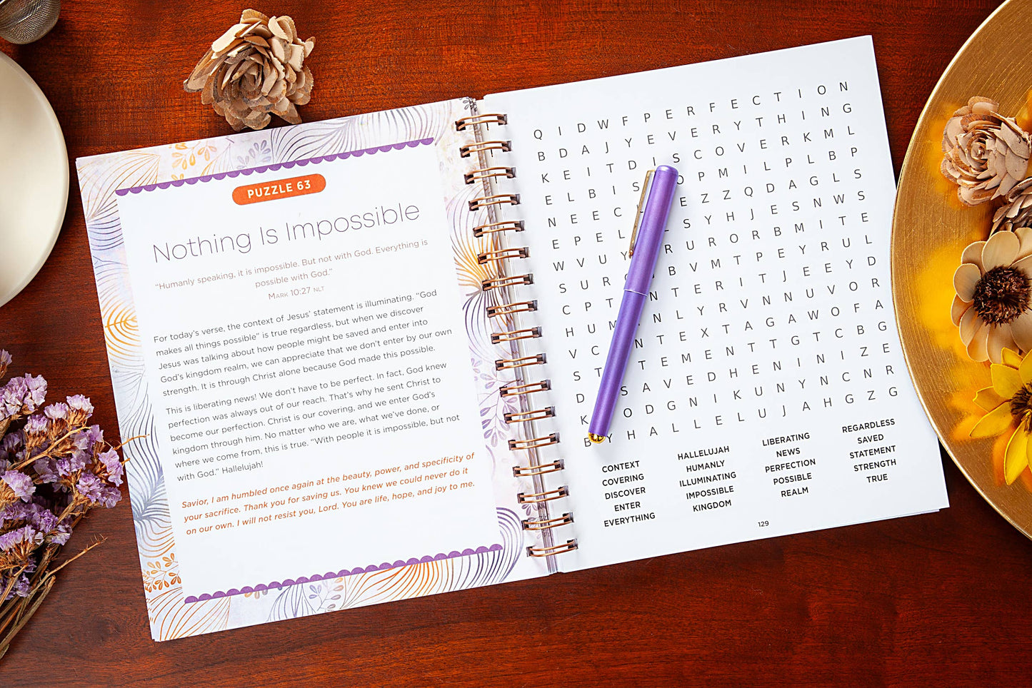 Large print open devotional word search book on a table with  various objects surrounding the book.