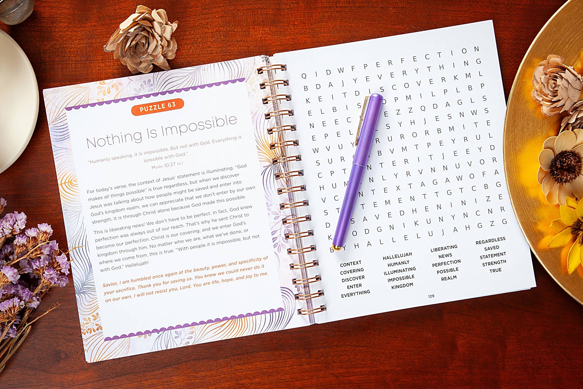 Large print open devotional word search book on a table with  various objects surrounding the book.