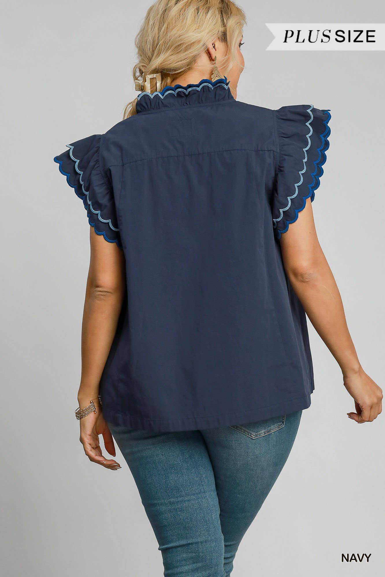 Woman wearing a navy blue blouse with ruffled sleeves on a gray background