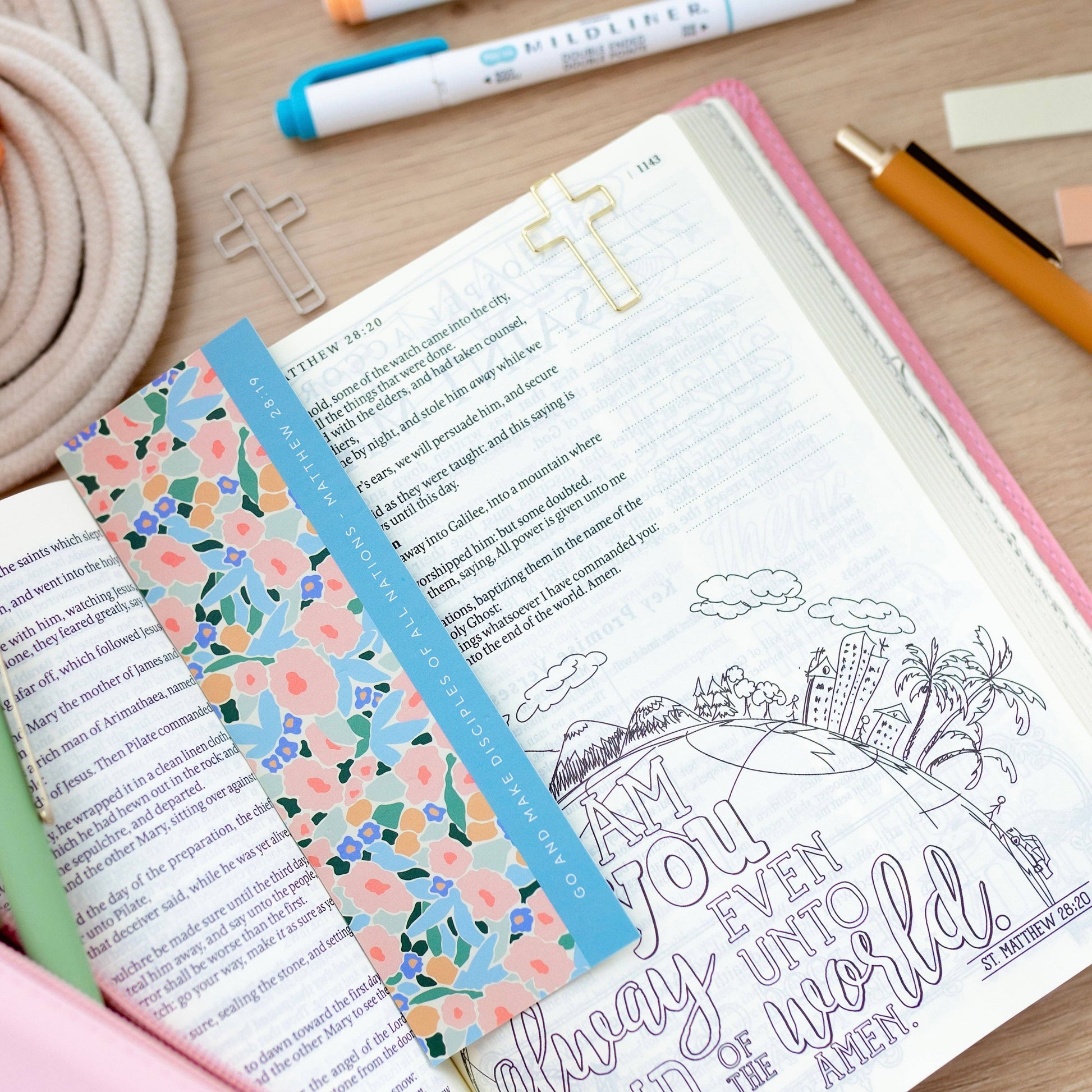 Open book with floral bookmark on a wooden surface with stationery items.