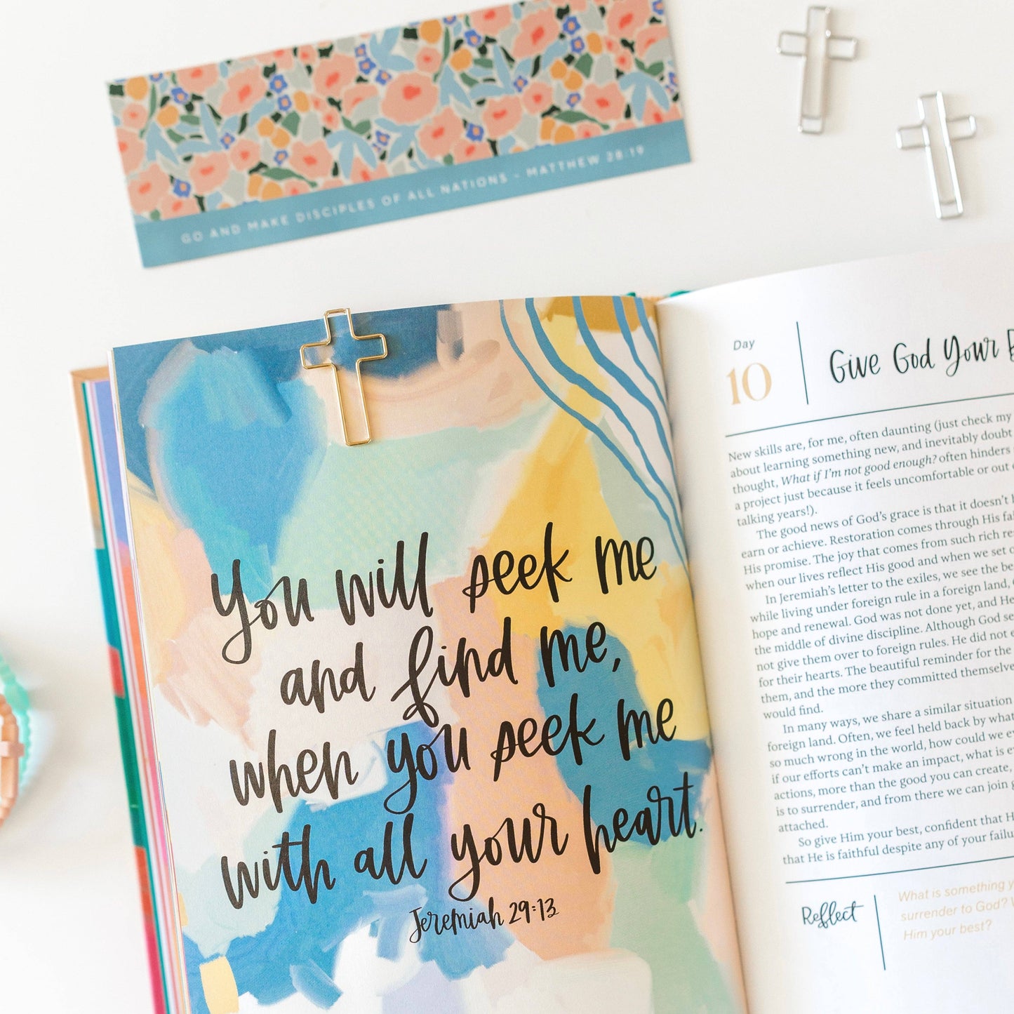 Open book with a pastel watercolor background and religious text, featuring a cross bookmark.