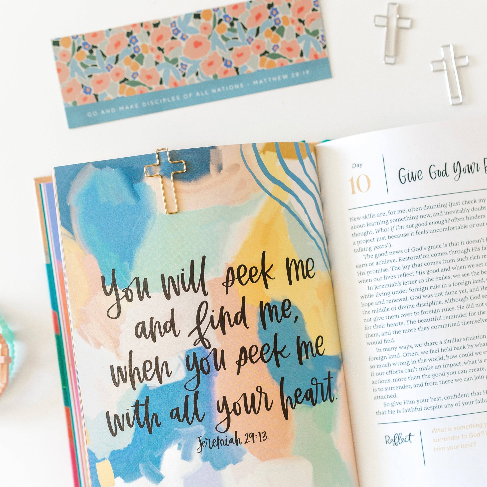 Open book with a pastel watercolor background and religious text, featuring a cross bookmark.