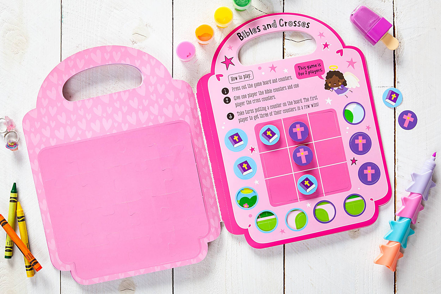 Children's pink activity books on a wooden surface with crayons and stickers.