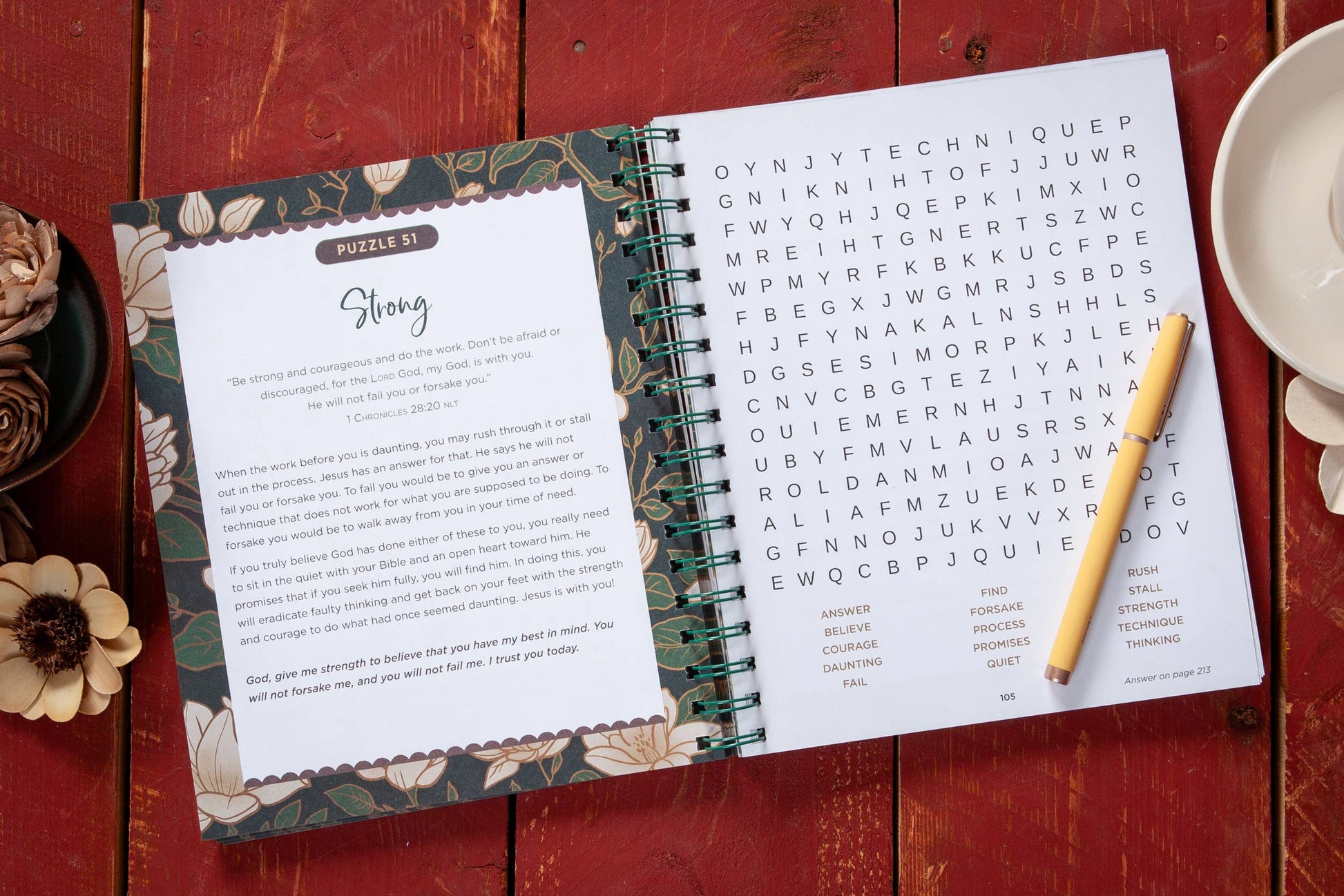 Large print open floral devotional word search book on a table with  various objects surrounding the book.