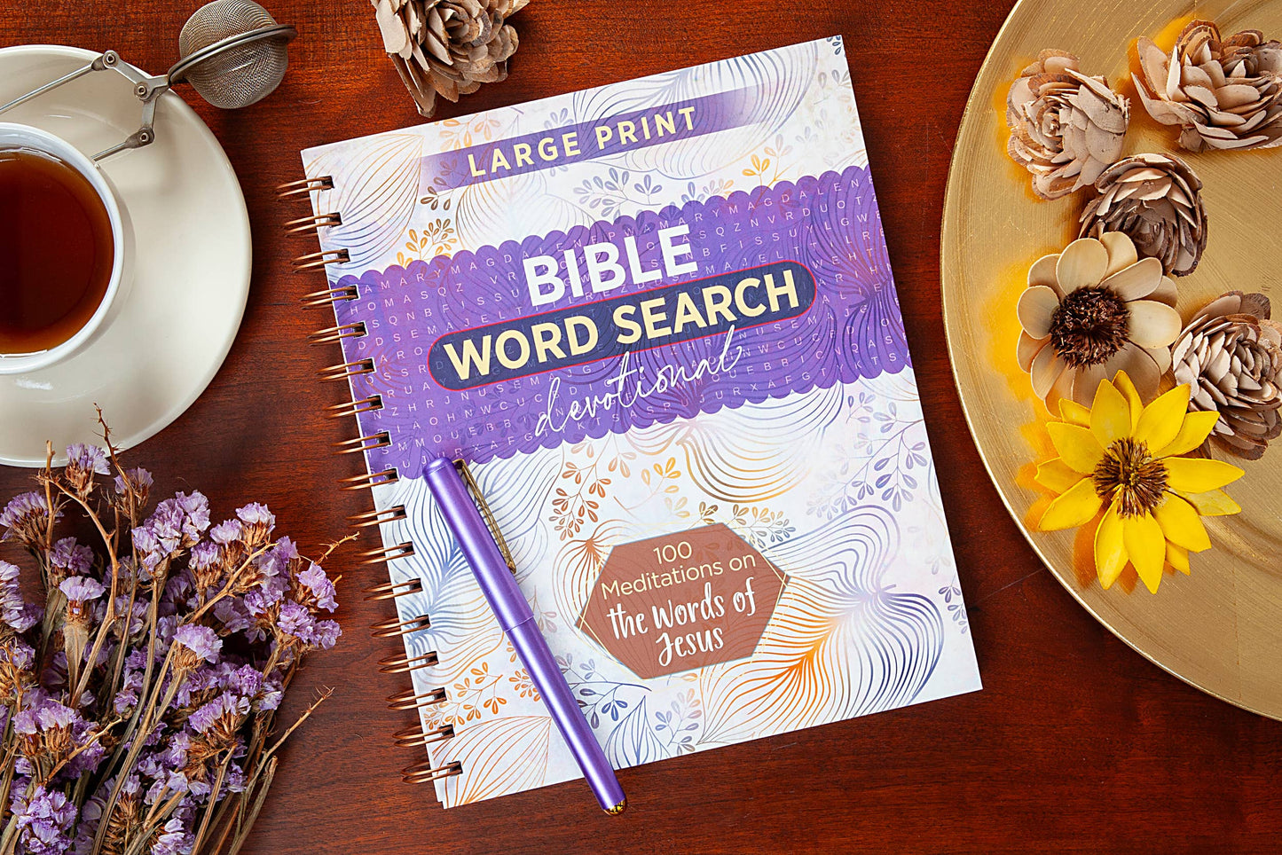 Large print devotional word search book on a table with  various objects surrounding the book.