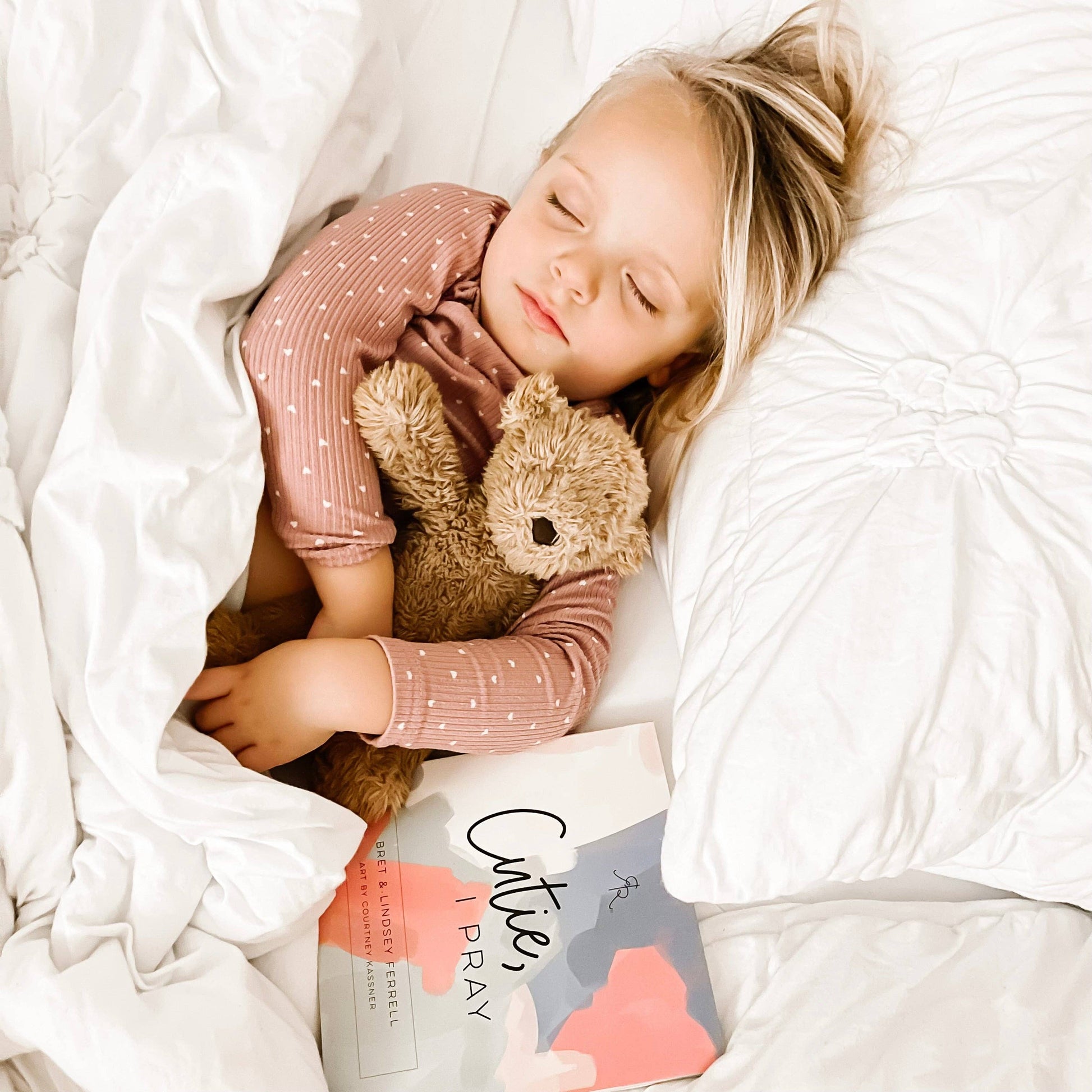 Child sleeping with a teddy bear under white bedding