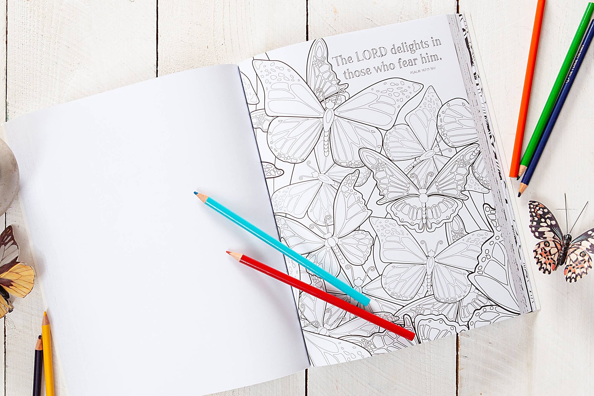 Coloring book with a floral design and text, surrounded by colored pencils on a wooden surface.