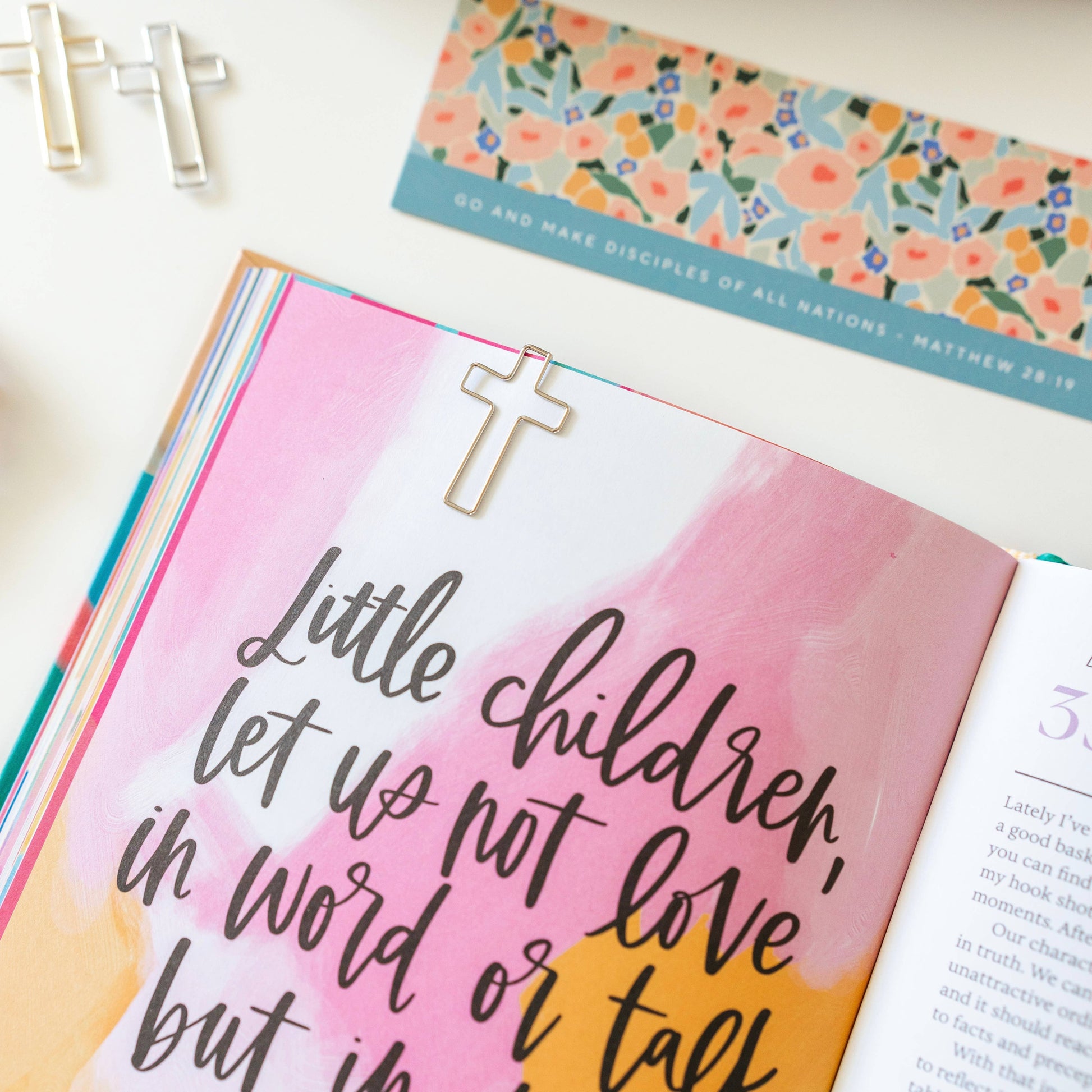 Open book with a pink watercolor background and religious text, featuring a cross bookmark.