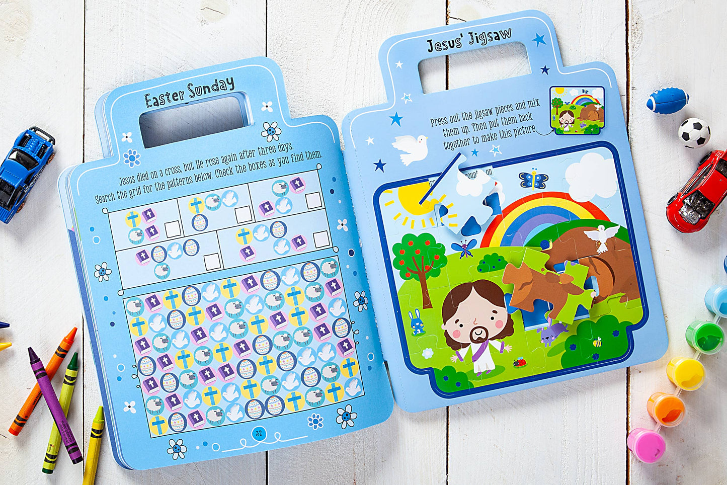 Blue children's activity books on a wooden surface with toys and crayons around.